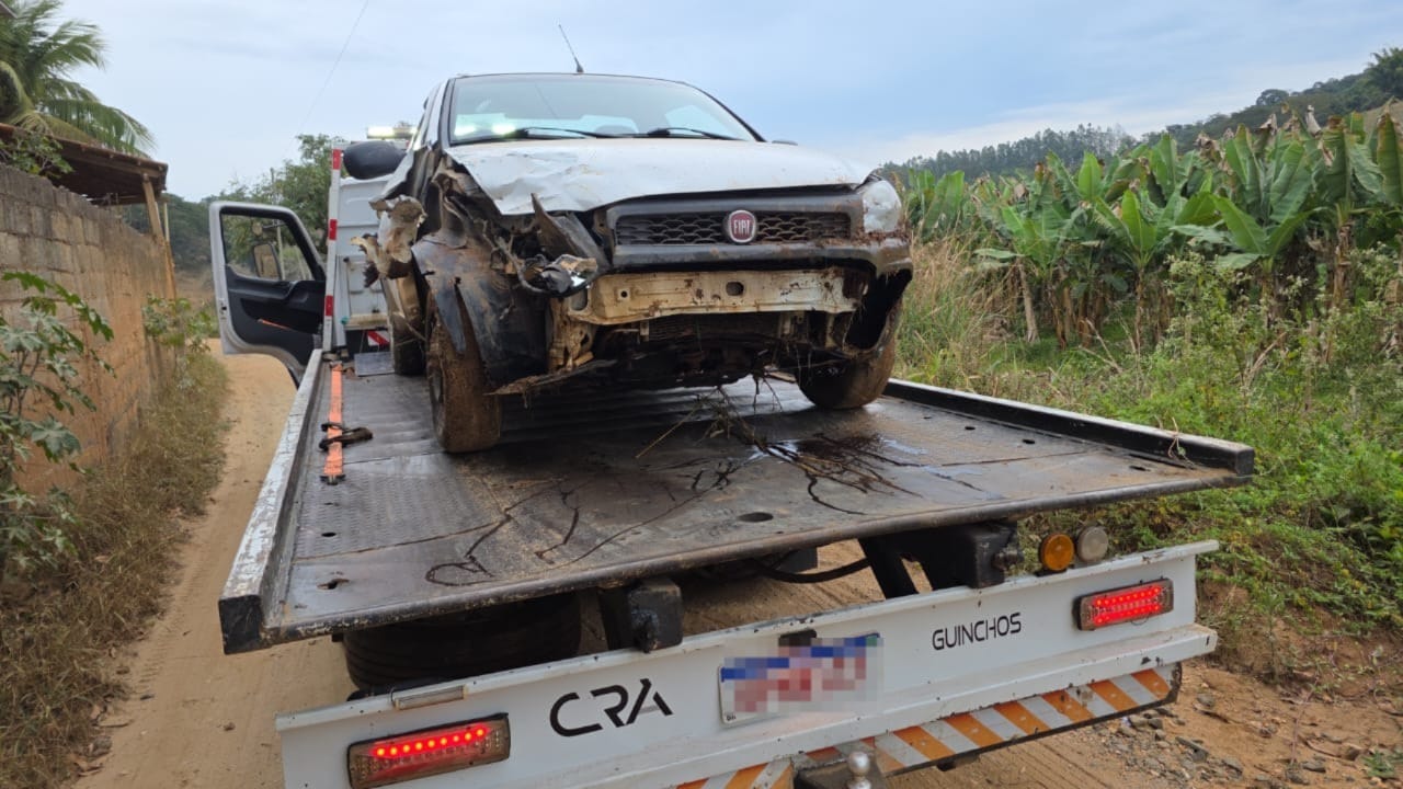 Carro com a frente destruída após acidente, carregado na plataforma da C.R.A Guinchos em estrada de terra